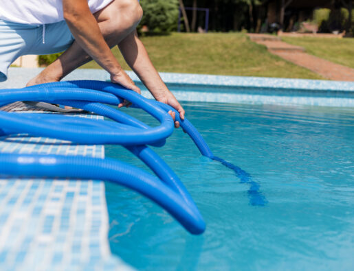 Mature man in flip flops cleaning the swimming pool with a vacuum cleaner.  Man working as a cleaner of the swimming pool, he standing with special equipment for cleaning at poolside and working